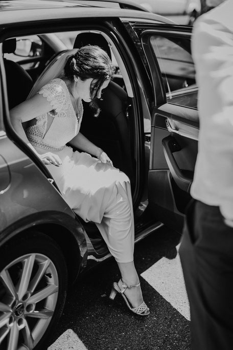 Schwarzweissbild einer Braut, die gerade aus einem Auto steigt