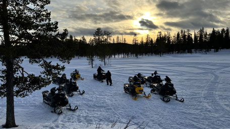 Schneemobile auf Waldlichtung mit wolkigem Sonnenuntergang