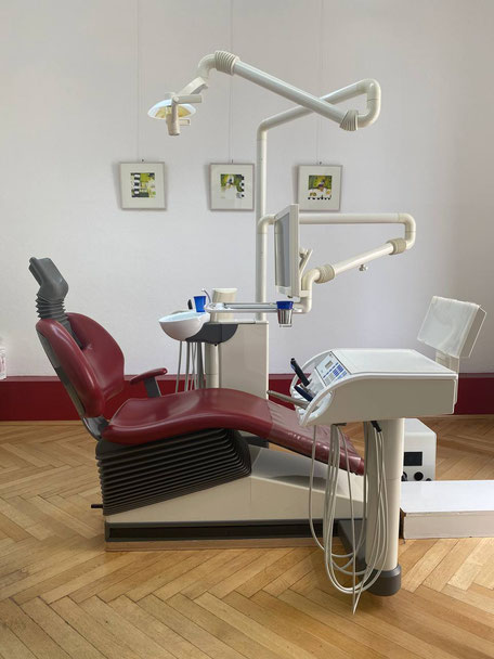 Behandlungszimmer 2 der Zahnarztpraxis Doumit mit Blick auf den roten Behandlungsstuhl. An der Wand hängen drei kleine Bilder.