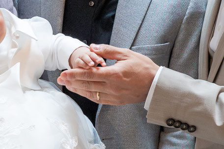 Ein zartes Detailbild: Die kleine Hand eines Täuflings ruht vertrauensvoll in der Hand des Vaters. Ein berührender Moment der Verbundenheit und Liebe während der Tauffeier.