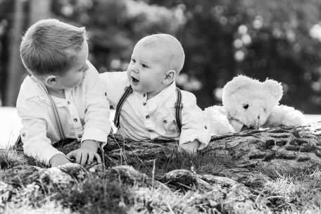 Verspieltes Outdoorshooting – zwei Jungs liegen entspannt an einem Baumstamm im Park, natürliches Kindershooting in der Natur