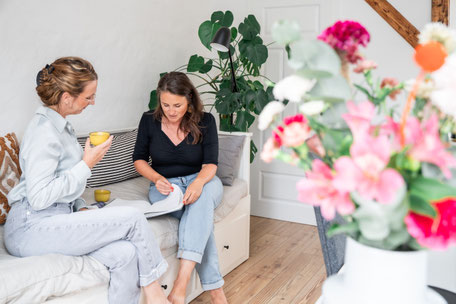 Zwei Frauen sitzen gemeinsam im Büro, während eine im Kalender blättert. Ein Moment der Planung und Organisation – ideal für Social Media, Business und Web