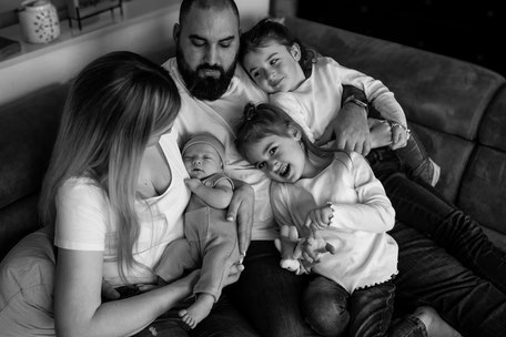 Eine fröhliche Familie kuschelt und lacht gemeinsam auf der Couch. Ein authentischer Moment voller Nähe, Liebe und unbeschwerter Freude in entspannter Atmosphäre.