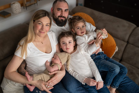 Eine liebevolle Familie mit drei Töchtern kuschelt eng beieinander auf der Couch. Ein inniger Moment voller Geborgenheit, Wärme und Zusammenhalt in heimischer Atmosphäre