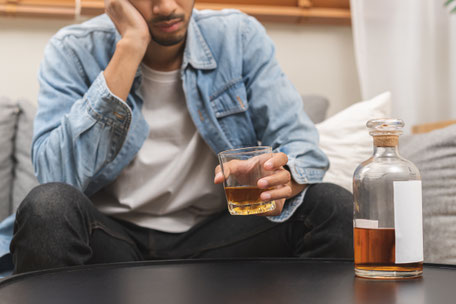 Ein Mann sitzt auf dem Sofa vor einer Flasche Alkohol
