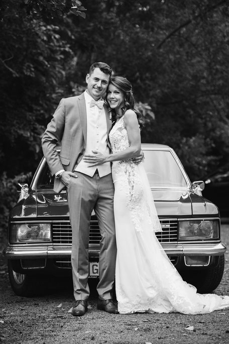 Hochzeitsfoto mit Brautpaar vor Auto in schwarz weiß
