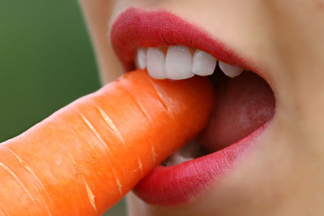 Junge Dame mit weißen Zähnen beißt in eine Karotte