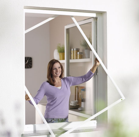 Frau zeigt im geöffneten Fenster einen leeren Spannrahmen als Befestigung für Insektenschutz