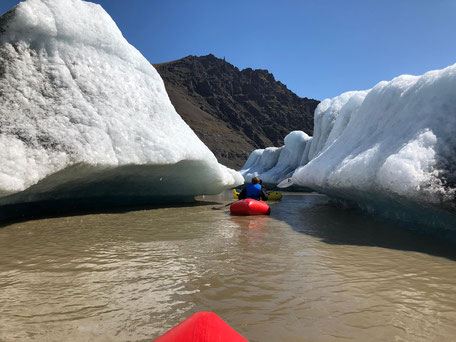 aufblasbare rote Kayaks inmitten der Eisberge in der mit braunem Wasser gefüllten Gletscherlagune