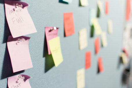 Bild zeigt Post-it Zettel an einer Wand, vorne scharf im Hintergrund verschwommen