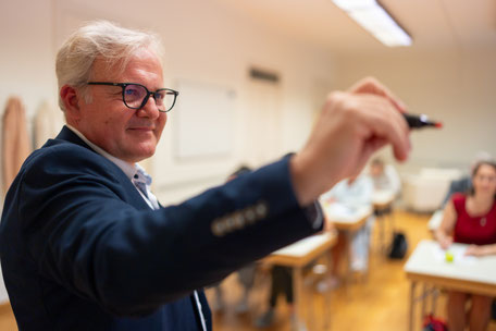 Martin Rotter vor einer Gruppe Teilnehmer:innen mit einem Stift in der Hand.