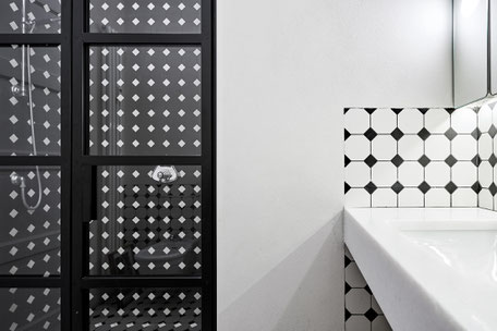 Un secondo bagno ha un mood più decorativo e gioca con grafiche black&white, con piastrelle in grès tinte in pasta che tra positivo e negativo rivestono la parete interna della doccia e la zona lavabo.