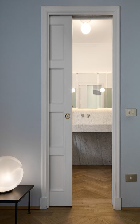 Vista del bagno en suite, una rigorosa composizione in marmo di Carrara con specchieta/contenitore su disegno e pannelli con applique incastonate.