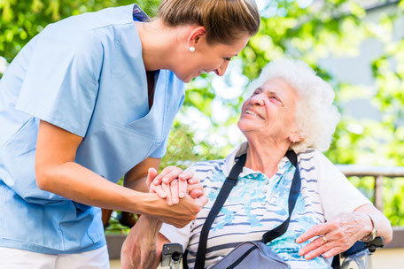 Symbolfoto: Eine weibliche Pflegekraft hält die Hand einer lächelnden Seniorin
