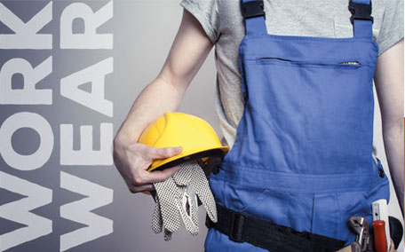 Person in blauer Latzhose hält gelben Bauhelm und Arbeitshandschuhe, daneben der Schriftzug „WORK WEAR“.