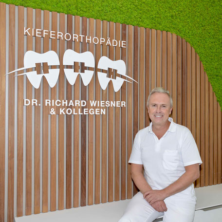 Dr. Richard Wiesner sitzt an der Rezeption der Praxis für Kieferorthopädie München Freimann.