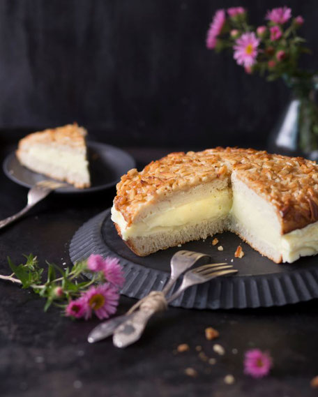 Bienenstichtorte mit Vanillecremefüllung und Mandelblättchen, ein Stück auf einem Teller daneben