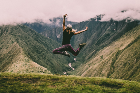 Ein junger Mensch springt befreit vor einem schönen Bergpanorama in die Höhe
