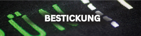 Nahaufnahme einer grünen Stickerei auf schwarzem Stoff mit erkennbarer Textstruktur und weißer Zierlinie, mit der Überschrift "Bestickung".