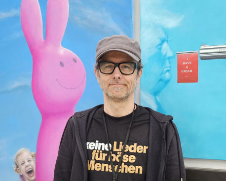 Christian Ristau vor zwei Bildern von Donald Trump und einem kleinen Mädchen mit einem Luftballon