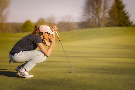 Golfspielerin kniet auuf dem Rasen und schaut in Richtung Loch