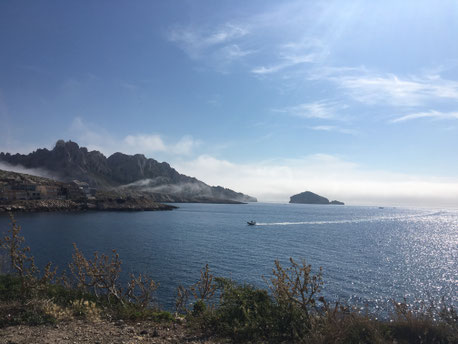 le calanques di Marsiglia, grossi scogli con nebbia attorno  e un gommone all'orizzonte in mezzo al mare