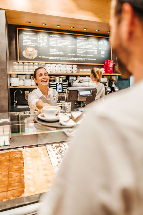 Bäckerei Verkäuferin reicht einem Kunden Kaffee und Kuchen über die Einkaufstheke