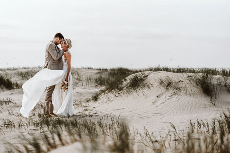 nach der freien Trauung mit Constanze Marienfeld steht Brautpaar innig in den Dünen von St. Peter Ording, das Brautkleid weht im Wind