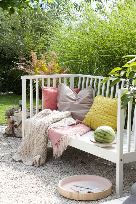 dieartigeBLOG - Weiße Gartenbank mit Kissen in Rosa und Limonengelb, Wolldecken, Melone, Holztablett, Kies-Terrasse