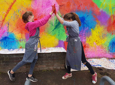 2 kinder amüsieren sich prächtig beim klecksen mit Farben bei der gestaltung einer Mauer in einem Kunstprojekt in der Schule