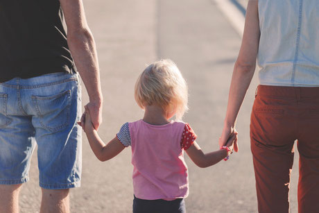 Familie mit 2 Kindern Hand in Hand auf dem Bürgersteig