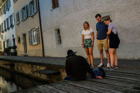 Das Bild zeigt eine Gruppe, welche eine Stadtführung in Sursee in Form einer interaktiven Schnitzeljagd machen. Es sind 3 Personen zu sehen, welche mit einem Schauspieler interagieren.