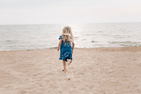Kleines Mädchen rennt barfuß am Strand den Wellen entgegen.