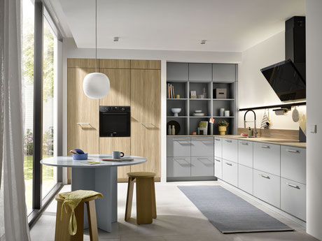 Helle, moderne Einbauküche mit viel Stauraum, grauen Fronten, Holzakzenten und gemütlichem Essbereich am runden Tisch – freundliches Küchendesign mit großem Fenster.
