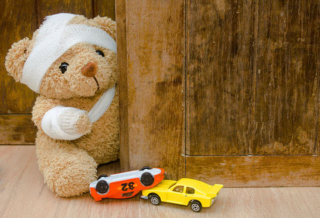 Teddybär mit Verband und Spielzeugwagen auf Holzhintergrund mit Kopienraum, Unfallkonzept.