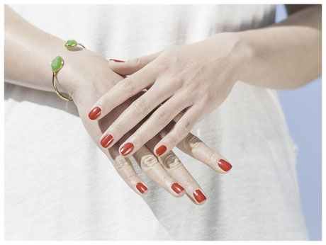 Gepflegte Frauenhände mit roten Nägeln und einem goldgrünen Armband.