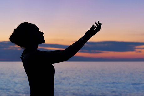 Silhouette of a woman in yoga pose in front of a beautiful sky and sea