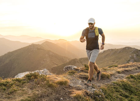 Ein Läufer rennt beim Sonnenaufgang auf einem Bergpfad Richtung Gipfel