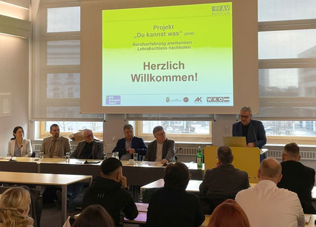 Begrüßung der Teilnehmer:innen durch das Organisationsteam vor einer Projektionswand