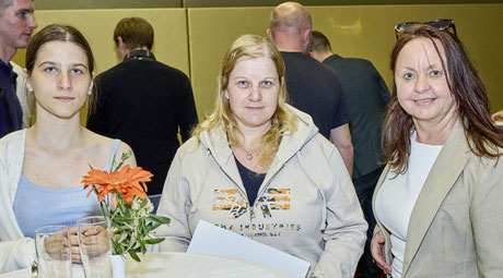 Drei Frauen, eine mit Urkunde, am Stehtisch bei der Feier