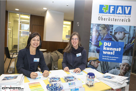 Zwei Mitarbeiterinnen am FAV OÖ-Stand im Gespräch, Infomaterial vor ihnen ausgebreitet