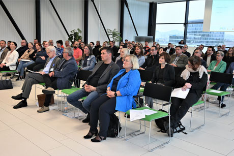 Teilnehmende sitzen aufmerksam in mehreren Reihen und hören einem Vortrag zu.