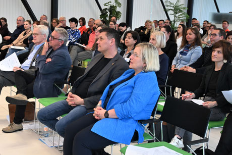 Reihe von Gästen, darunter mehrere Frauen und Männer mittleren Alters, sitzen konzentriert während eines Vortrags.