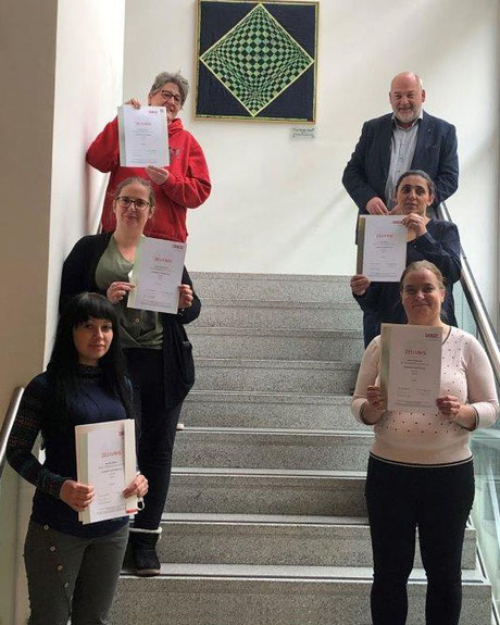 Weitere Absolvent:innen präsentieren ihre Lehrabschlusszeugnisse auf einer Treppe, begleitet von einem Vertreter der Organisation