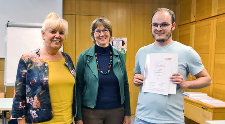 Zwei Gratulantinnen posieren gemeinsam mit Teilnehmer im Seminarraum