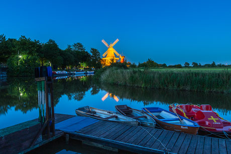 Blaue Stunde in Greetsiel mit den beleuchteten Zwillingsmühlen  und Tretbooten im Vordergrund 