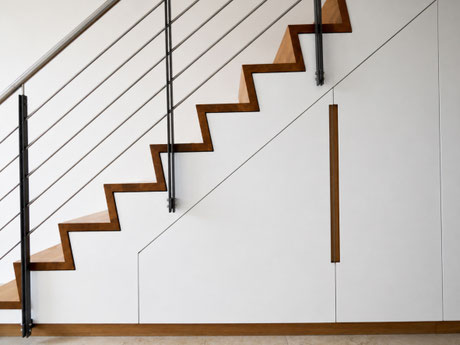 Garderobenschrank nach Maß unter einer Faltwerktreppe. Die innenliegende Garderobe nutzt den Raum unter der Treppe als Stauraum für Jacken, Taschen und Schuhe und greift die Eiche-Treppenstufen mit flächenbündigen Griffleisten auf.