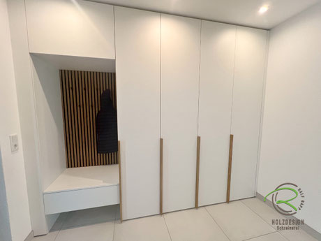 Maßgefertigte weiße Einbau-Garderobe für Stockach vom Schreiner mit Eiche-Nische und wandhängender Sitzbank, Eiche Griffleisten im Eingangsbereich
