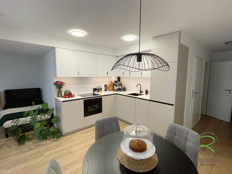 Kompakte Küche in weiß & beige über Eck im offenem Wohnraum einer Singlewohnung in Rottweil, mit schwarzen Desginelementen wie Griffleiste, Spülarmatur und Spülbecken