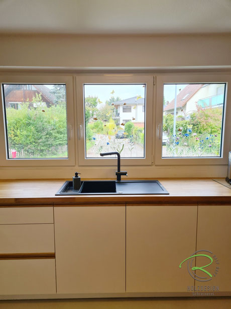 Küchenspüle mit schwarzer Armatur vor dreiteiligem Fenster, helle Unterschränke und Eichenarbeitsplatte in einer maßgefertigten Schreinerküche in Radolfzell-Markelfingen.